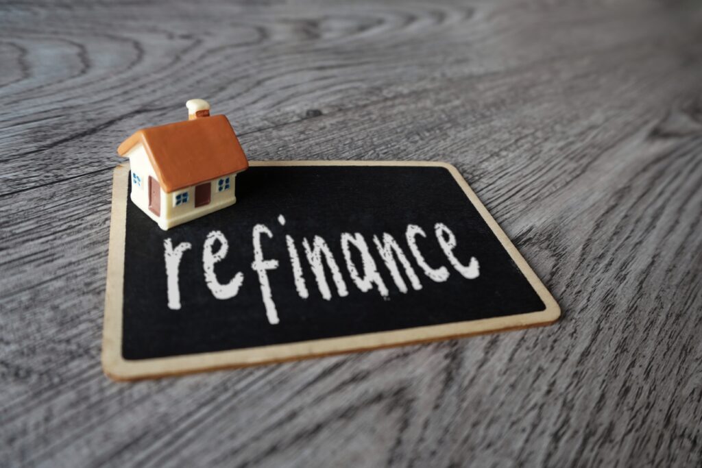 Small toy house next to wooden letter blocks spelling Refinance on a desk