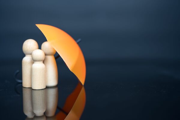 Wooden family figures sheltered under an orange umbrella
